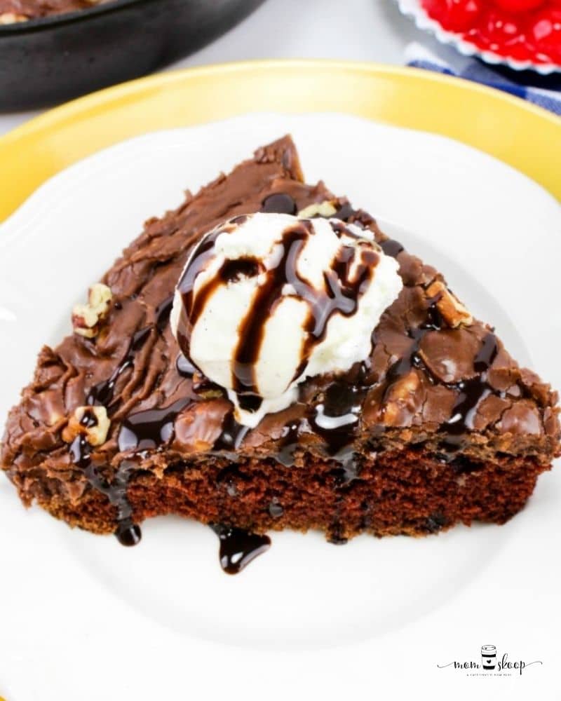 A slice of chocolate cake made in a cast iron skillet topped with ice cream and chocolate syrup