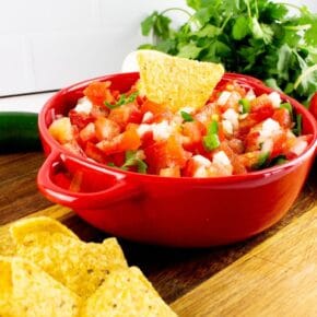 A red bowl full of fresh pico and a stack of corn tortilla chips