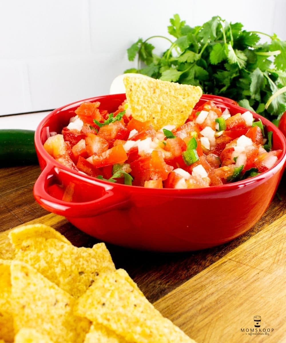 A red bowl full of fresh pico and a stack of corn tortilla chips