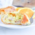 Quiche made with Puff Pastry, served with an orange, on a white plate.