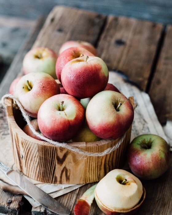 A wooden basket full of apples on a wooden board