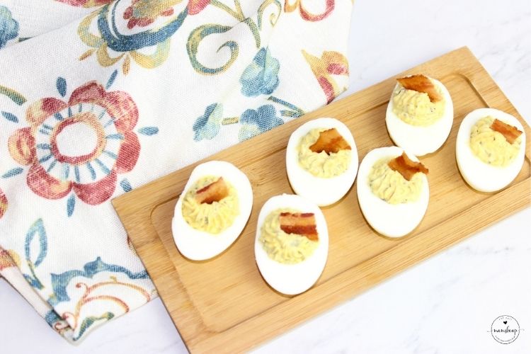 Hard boiled deviled eggs on a wooden bamboo serving tray next to a white napkin