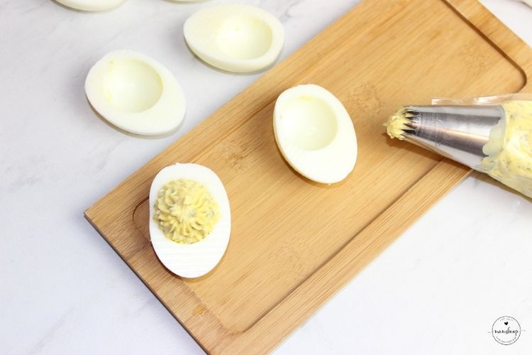 Piping deviled egg mixture into hard boiled eggs.