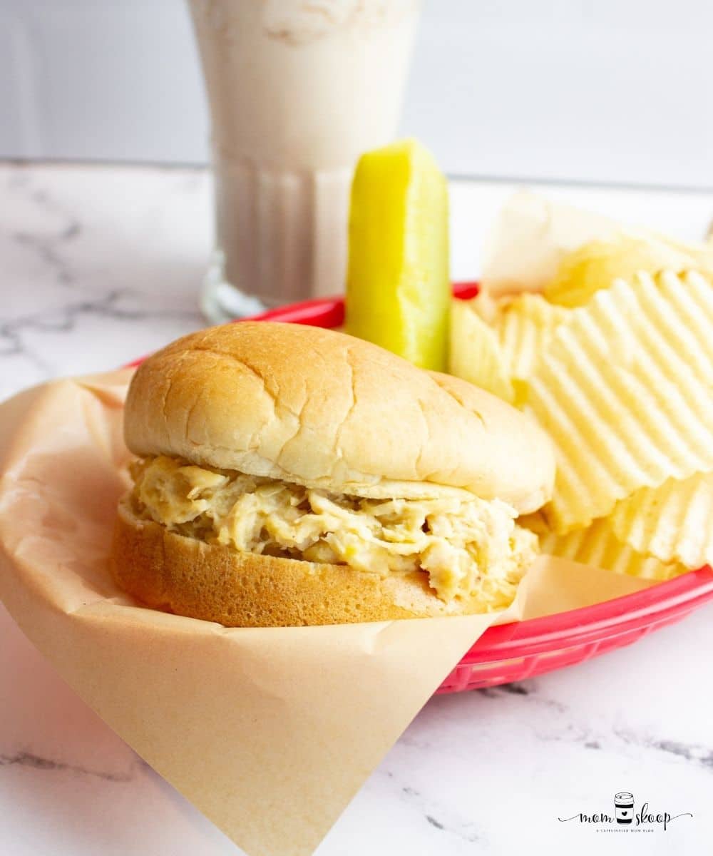 Shredded chicken inside a bun with chips and a dill pickle and milkshake