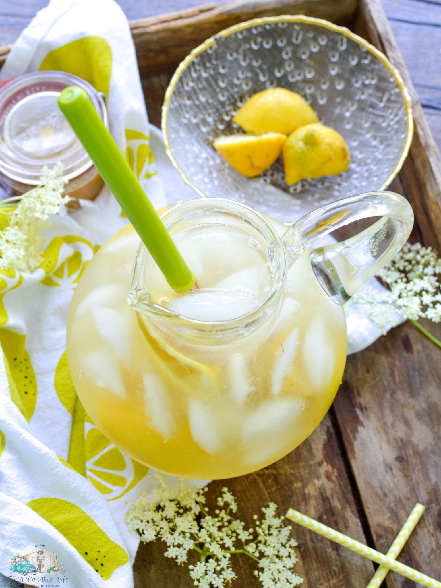 A glass pitcher of Elderflower Lemonade next to a bowl full of lemons