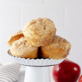 Cinnamon Muffin Melts stacked on a mini white cake stand with two red apples and a gray striped napkin