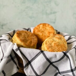 Three buttery biscuits in a bowl on top of a white napkin with black lines