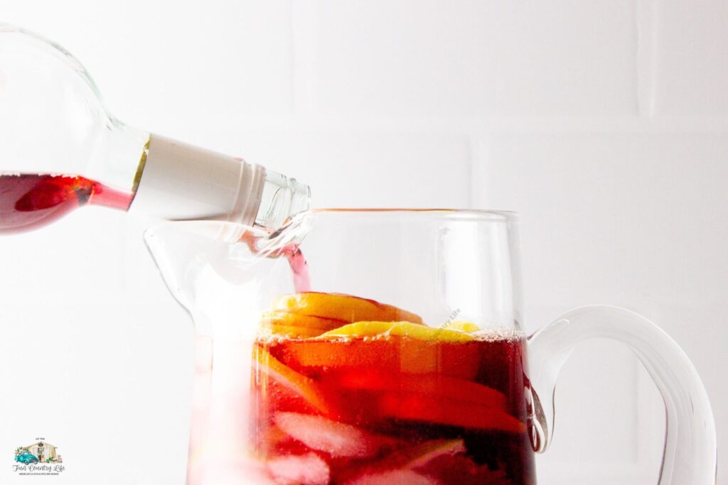 Pouring red wine into a glass pitcher full of fruit slices