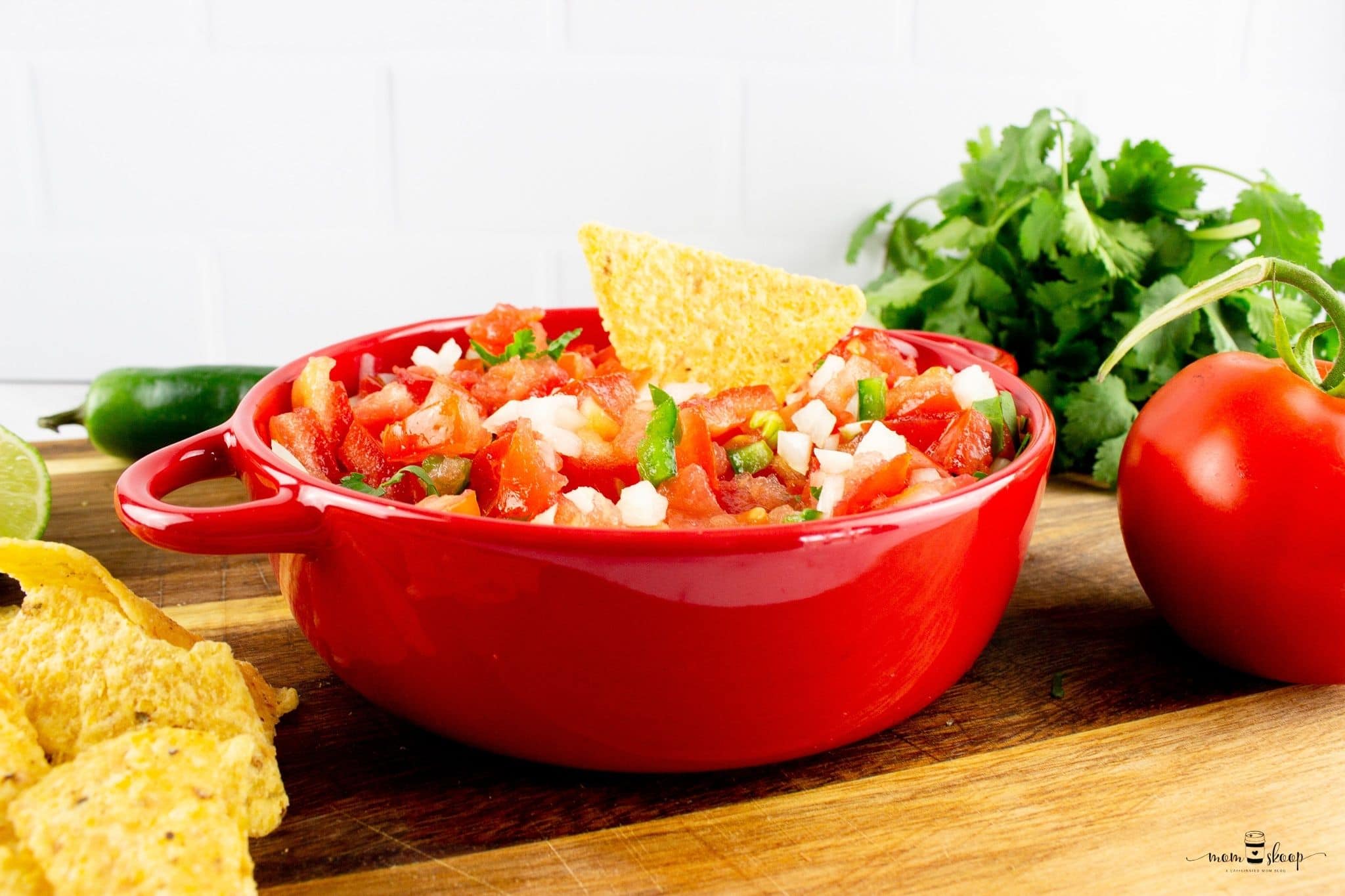 A red bowl full of fresh Pico de Gallo sitting on a wooden board 