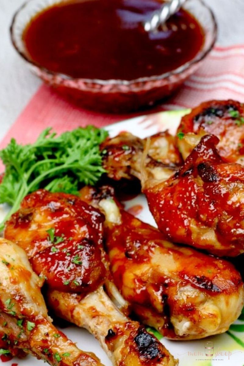 BBQ chicken legs on a plate with a bowl of bbq sauce nearby.