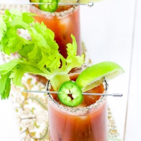 Celery sticks, lime wedge, jalapeno slice and a glass full of bloody mary cocktail
