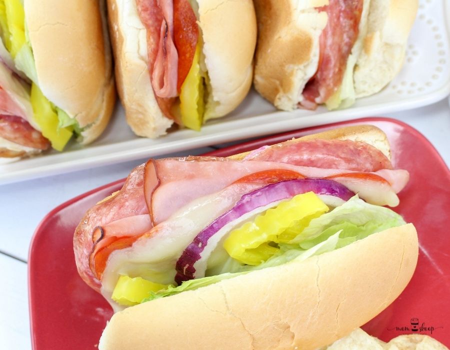 Ham, onions, tomatoes, lettuce, and peppers on a submarine bun on a red plate