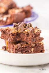 Two chocolate brownies topped with caramel and pecans on a white plate.