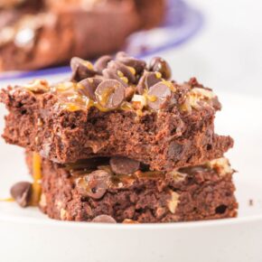 Two chocolate brownies topped with caramel and pecans on a white plate.