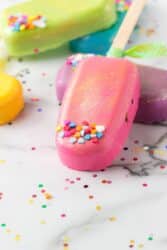 Rainbow cakesicles on a marble surface with sprinkles