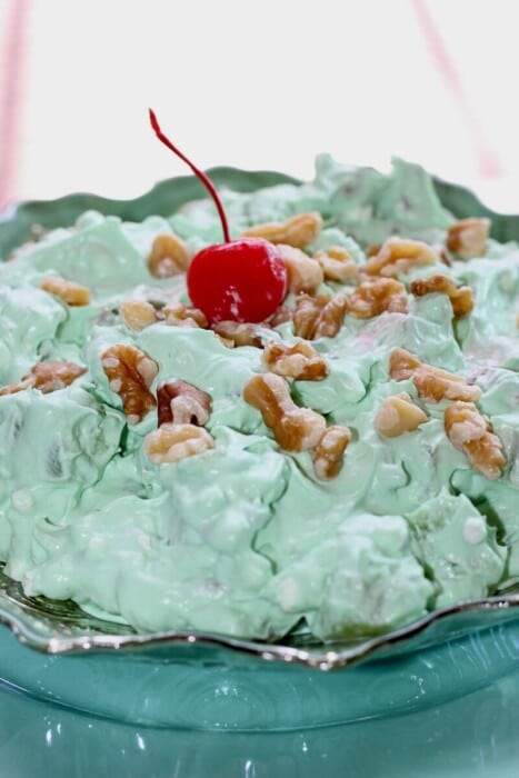 Lime Green Jello-O Salad in a bowl topped with walnuts and a cherry