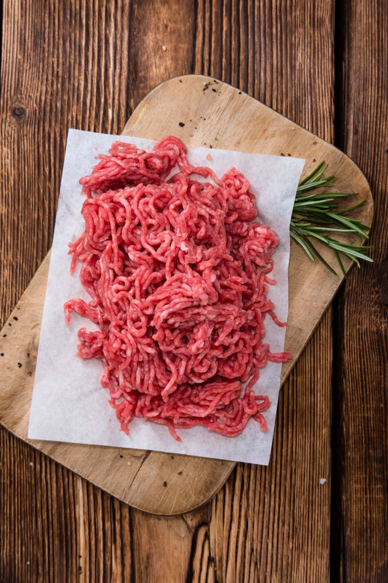 Hamburger meat on butcher paper on a wooden board.