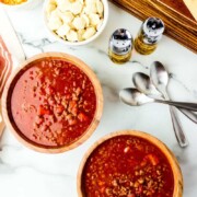 Two wooden bowls full of chili with ground beef, tomatoes, and kidney beans