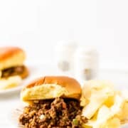 Loose meat with peppers, onions, and other ingredients on a white plate and with a bun.