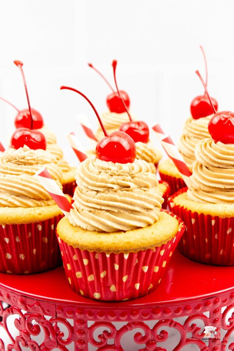 7 Root Beer float cupcakes with cherries and a straw sticking out of each cupcake.