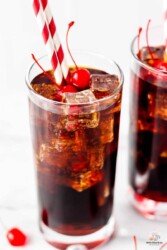 Coca Cola and Grenadine in a glass with maraschino cherries and two straws.