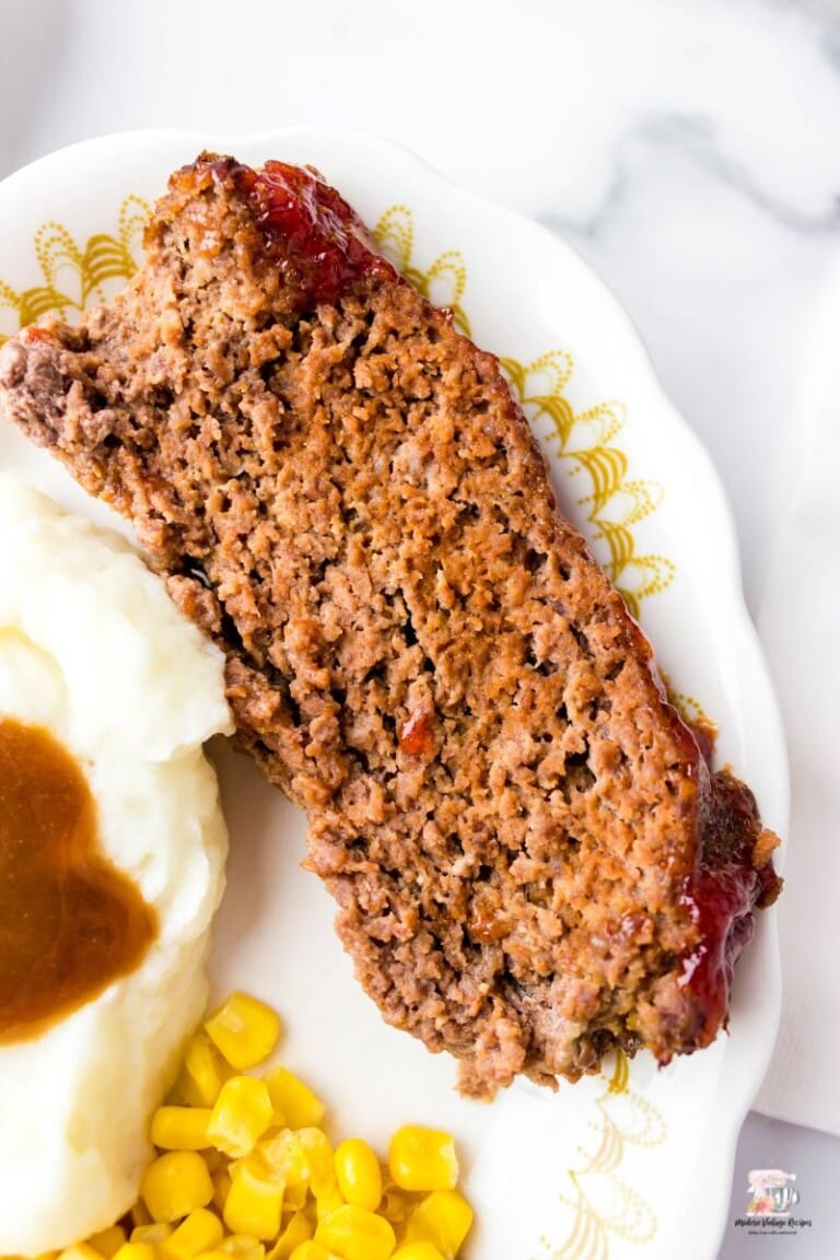 Tomato Soup Meatloaf on a white plate with mashed potatoes and gravy.