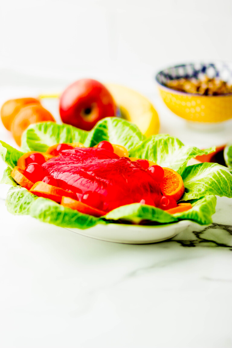 Fruit gelatin mold on top of lettuce and orange slices on a white plate.