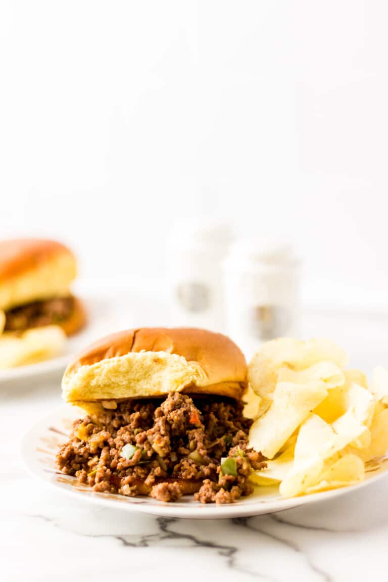 Classic Spoon Burgers on a bun served with chips on a white plate.